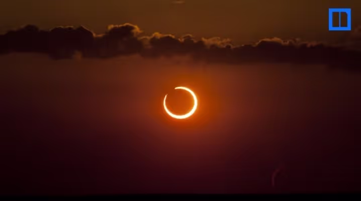 A wide-angle landscape photo of a "ring of fire" annular solar eclipse glowing in a dark orange sky with silhouetted clouds.