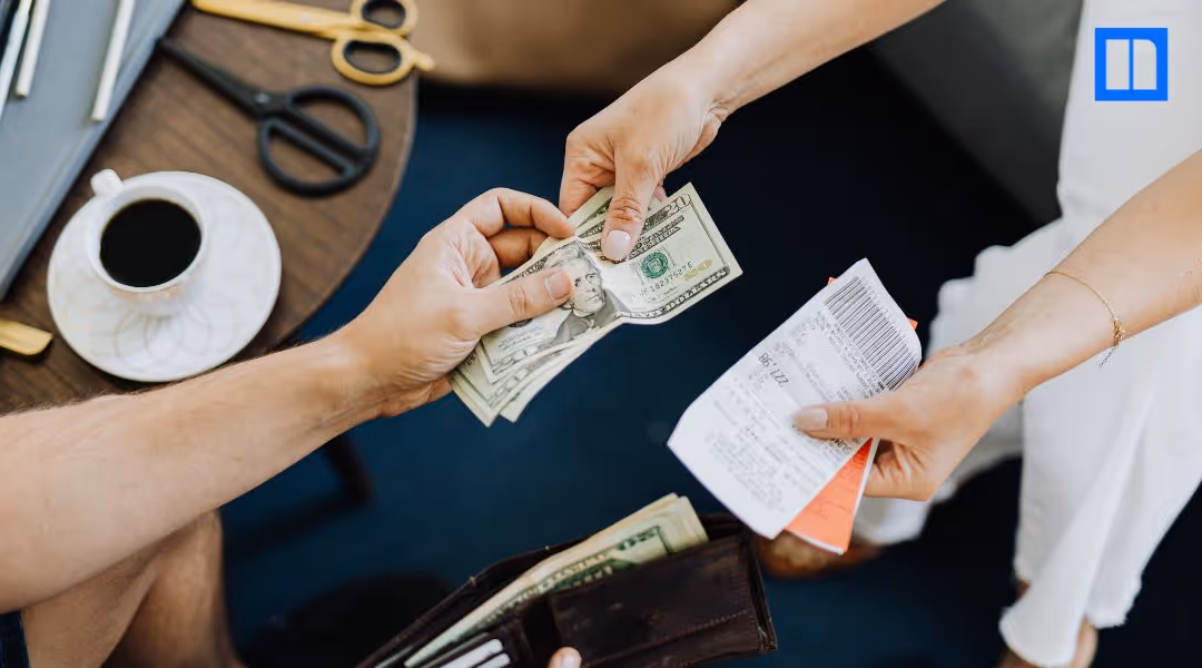 A customer hands cash to a cashier holding a receipt at a checkout counter.