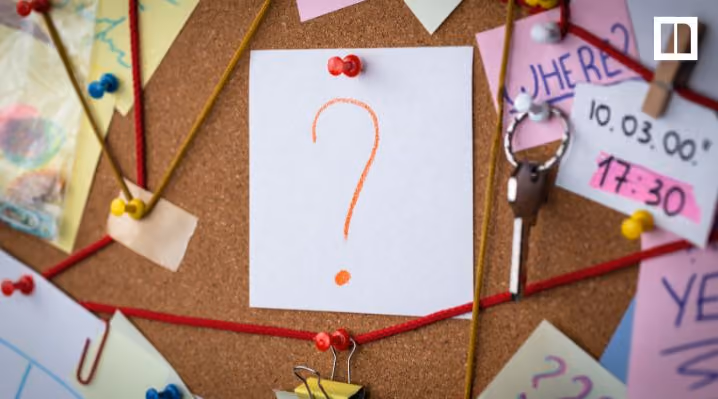 Corkboard with pinned notes, red string, and a paper showing an orange question mark.