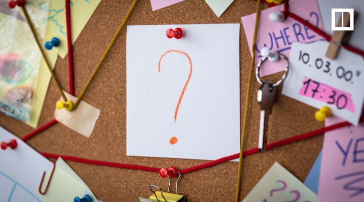 Corkboard with pinned notes, red string, and a paper showing an orange question mark.