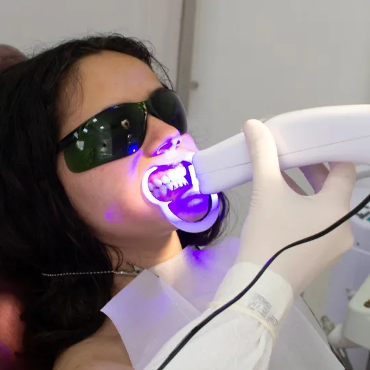 Patient undergoing professional teeth whitening with a blue LED light and protective eyewear.