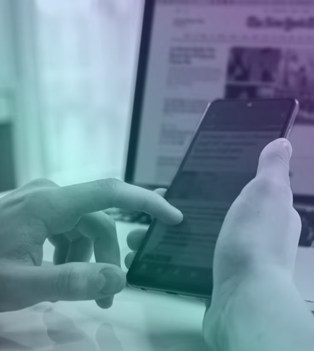 Person holding and interacting with a smartphone in front of an open laptop displaying a website.