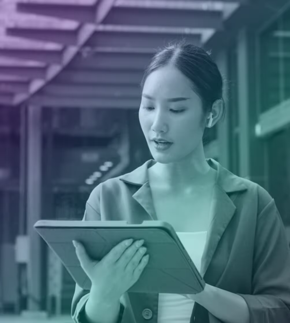 Young woman wearing wireless earbuds looking at and holding a tablet device indoors.