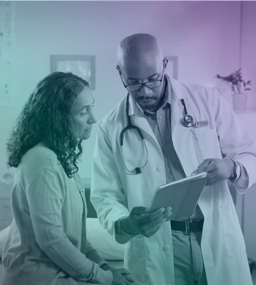 Doctor in white coat with stethoscope showing information on tablet to a seated female patient.