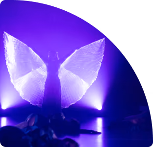 Danser met verlichte vleugels poseert op een podium met paarse verlichting.