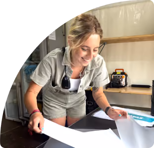 Vrouw glimlachend terwijl ze papier doorziet aan een tafel in een binnenruimte.