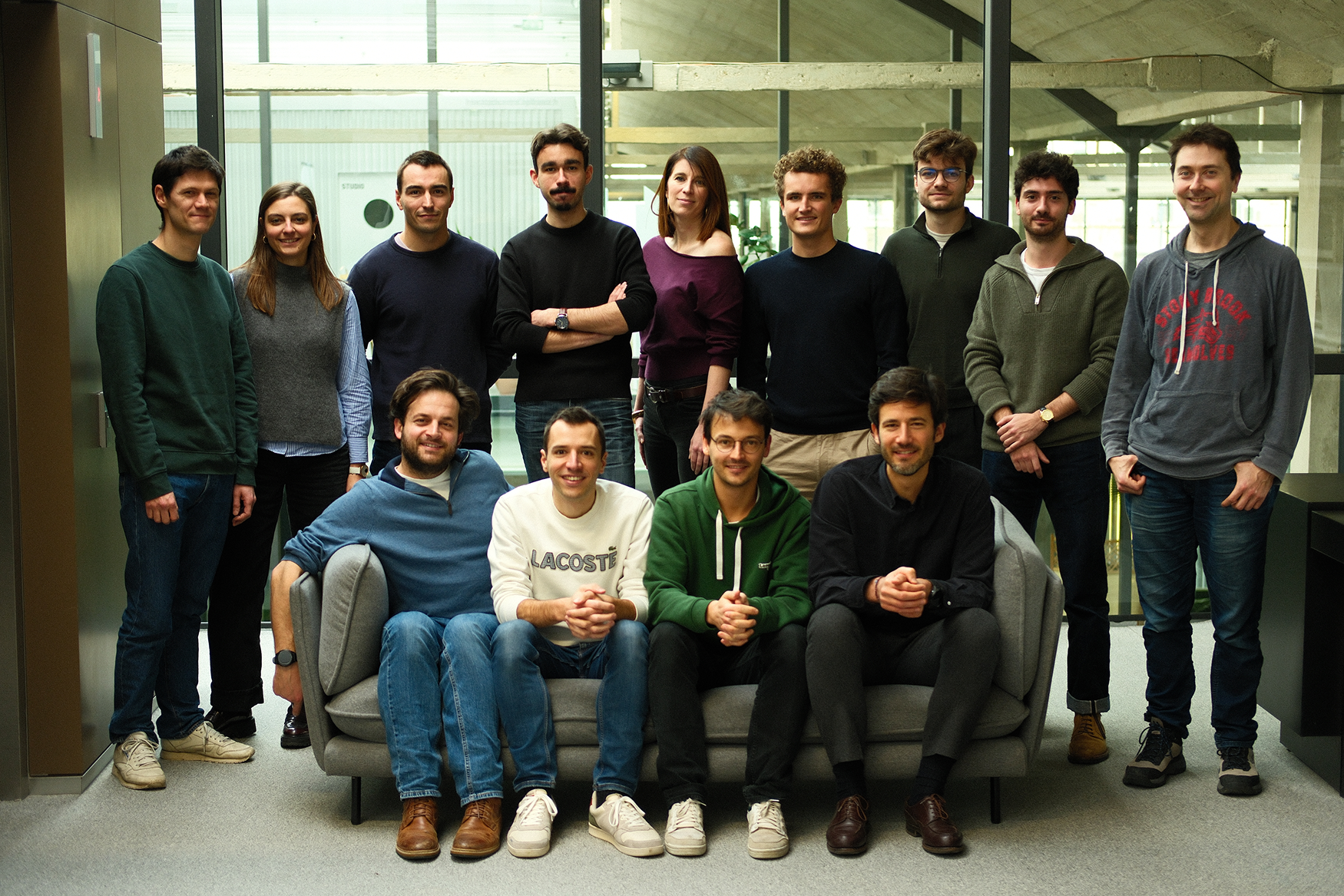 Group picture of the Neuralk AI team posing indoors with a modern architectural background.