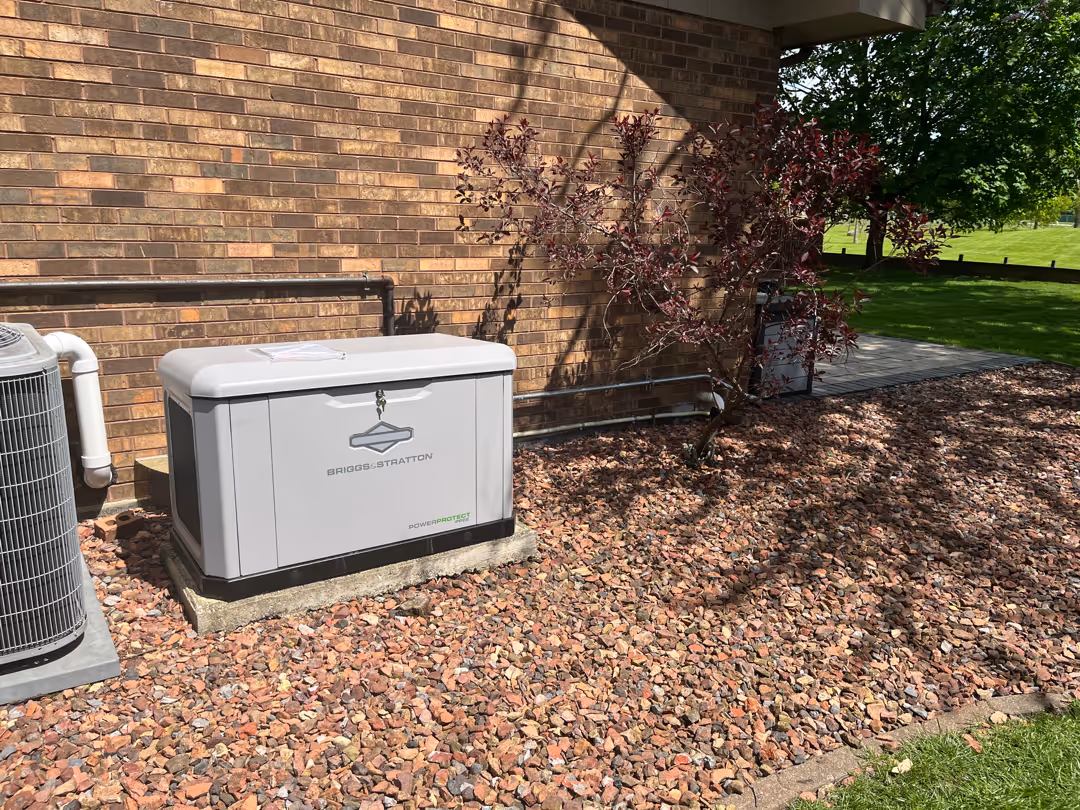 Briggs & Stratton standby generator installed on a concrete pad next to a brick house in a backyard.