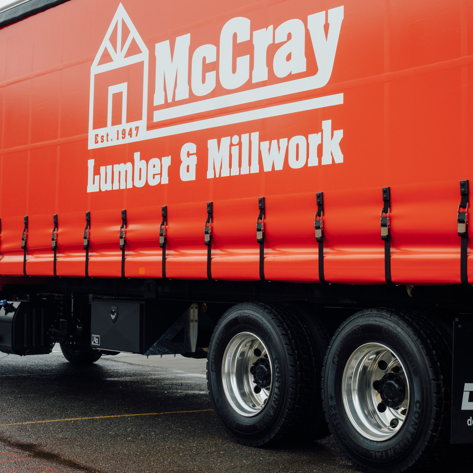 The side of a curtainside truck with a red curtain and the logo for McCray Lumber & Millwork on it.
