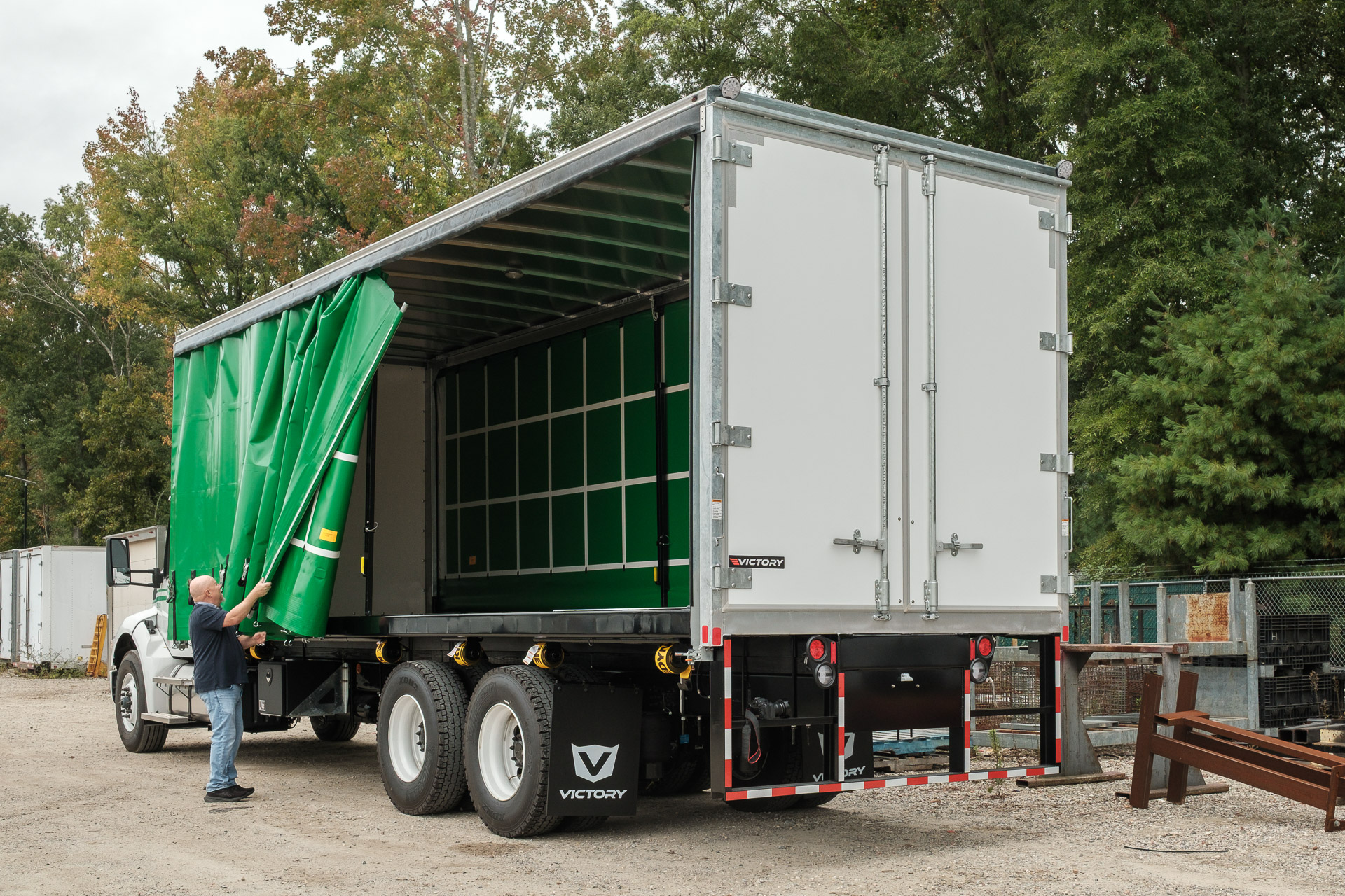 A man operating the driver's side curtain on a curtainside truck with green curtains.