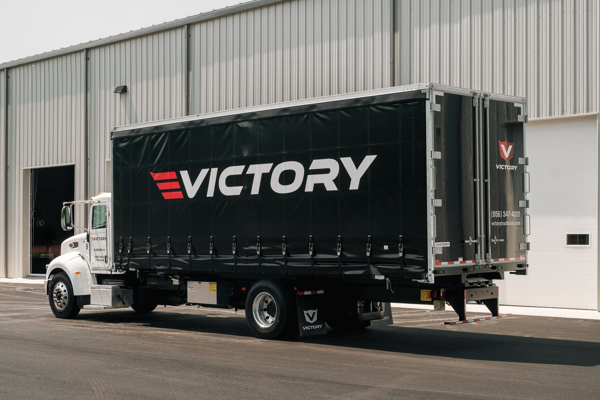 Victory curtainside truck with the curtain closed, parked in front of a warehouse.