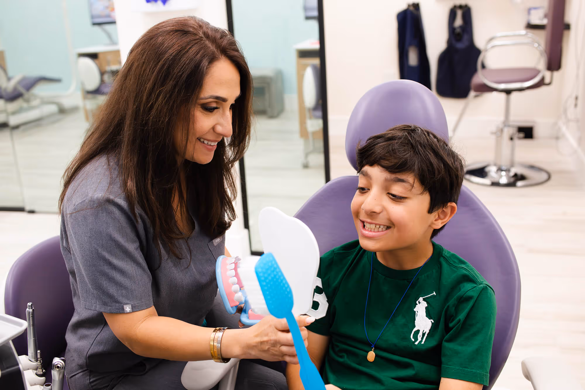 A woman showing a boy how to brush his teeth.