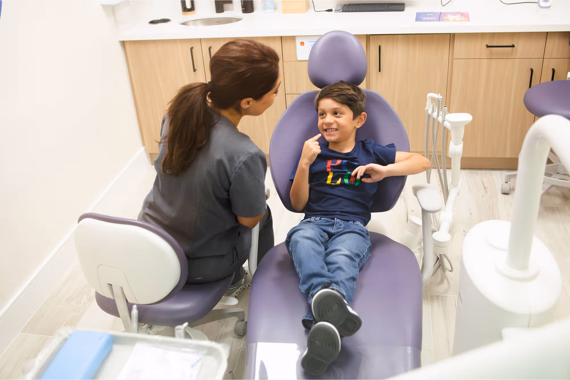 A young boy sitting on a purple chair in a dentist's office.