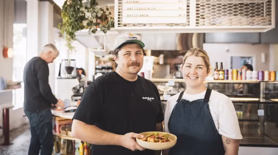 Local Hamilton café owners proudly present a beautifully prepared dish, showcasing fresh, organic ingredients. The warm atmosphere reflects community spirit, supporting Hamilton's vibrant local food scene and businesses.