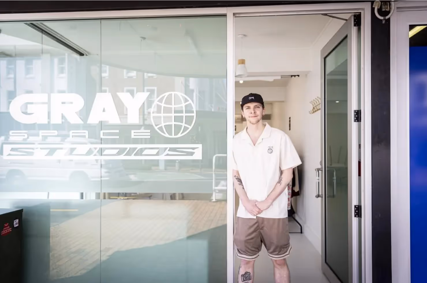 Alt text: "A smiling young man stands at the entrance of Gray Space Studios in Hamilton, showcasing the vibrant local business community. The studio features modern design and promotes creative experiences in the heart of the city."