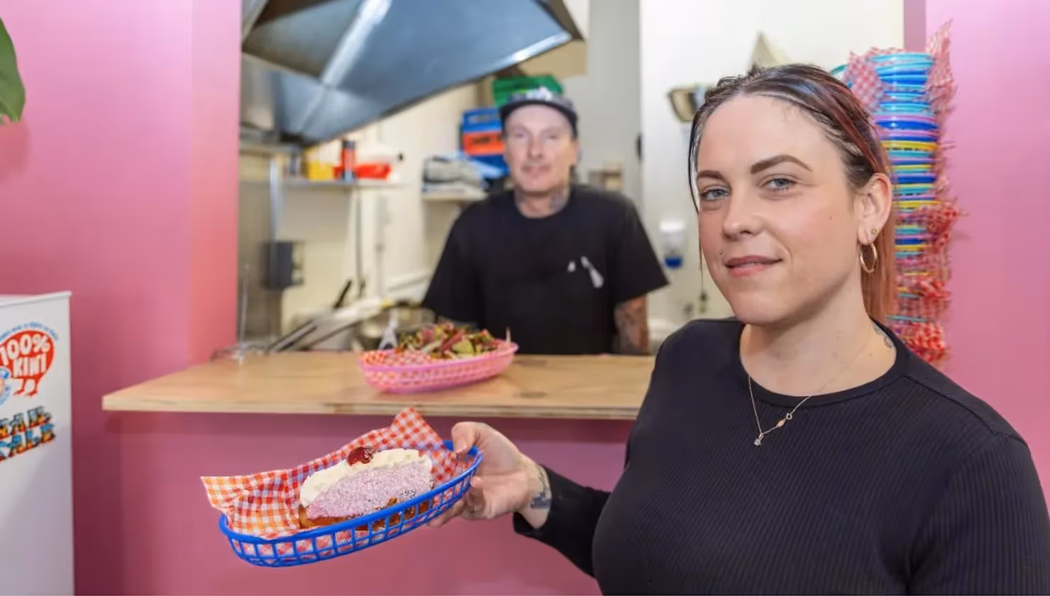 Alt text: A woman holding a delicious dish in a vibrant eatery, with a smiling chef visible in the background. Love the Centre champions local dining experiences in Hamilton, showcasing the best of the city's culinary scene.