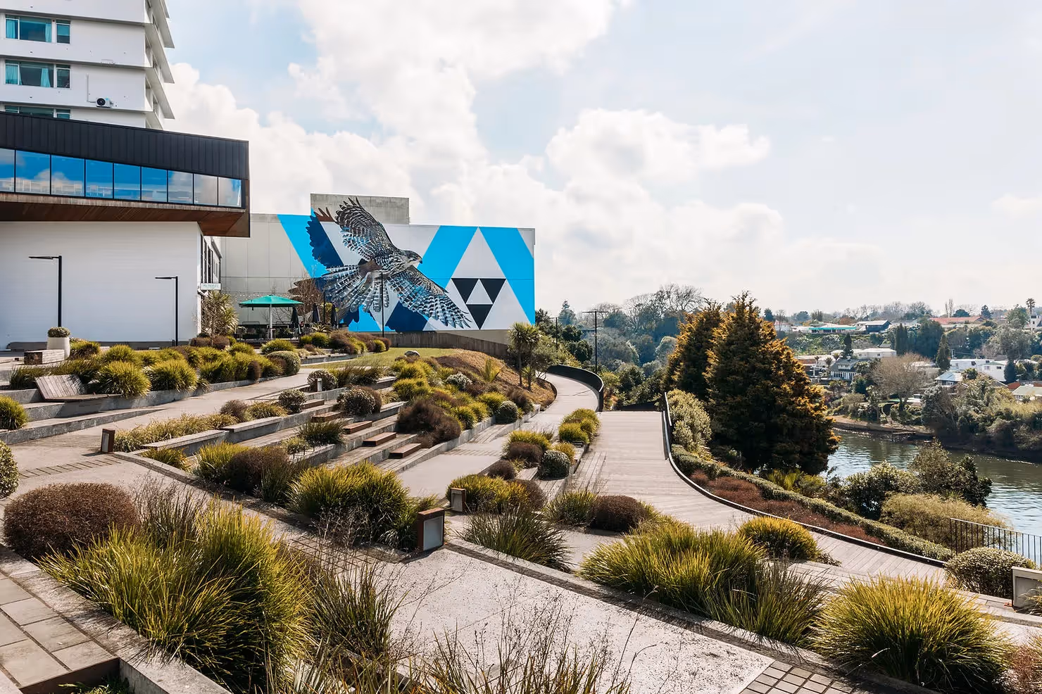 Alt text: Scenic view of Hamilton, featuring contemporary urban landscaping with lush greenery, a striking mural of an eagle, and the Waikato River in the background. A highlight of local culture and community in Hamilton’s vibrant heart.
