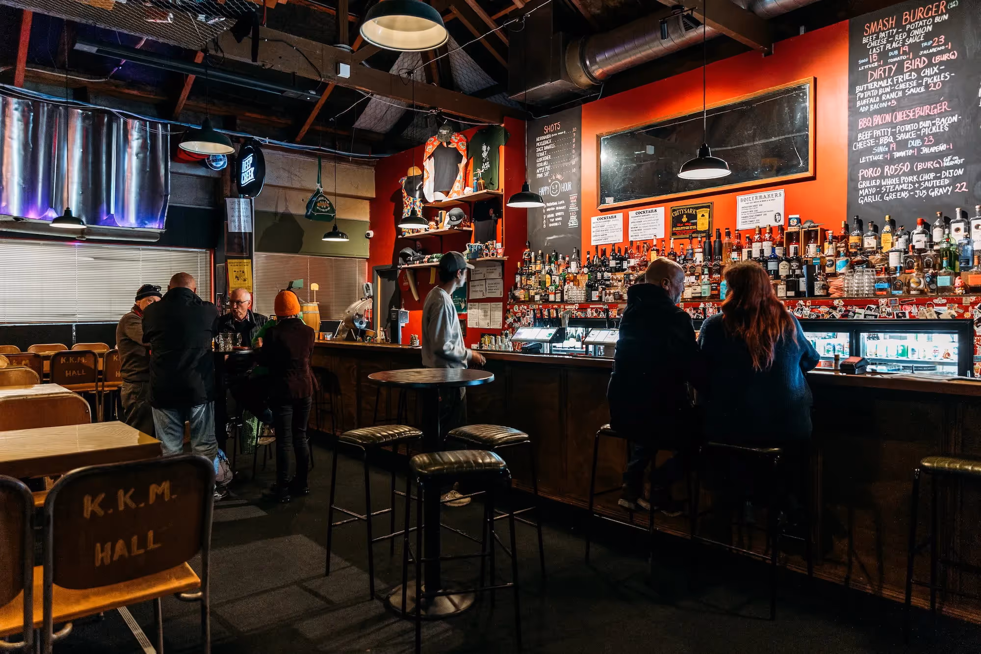 Alt text: "Interior of a vibrant Hamilton bar showcasing local spirits and craft beers. Patrons enjoy drinks at the counter and tables, highlighting the community atmosphere and support for local businesses in the heart of Hamilton."