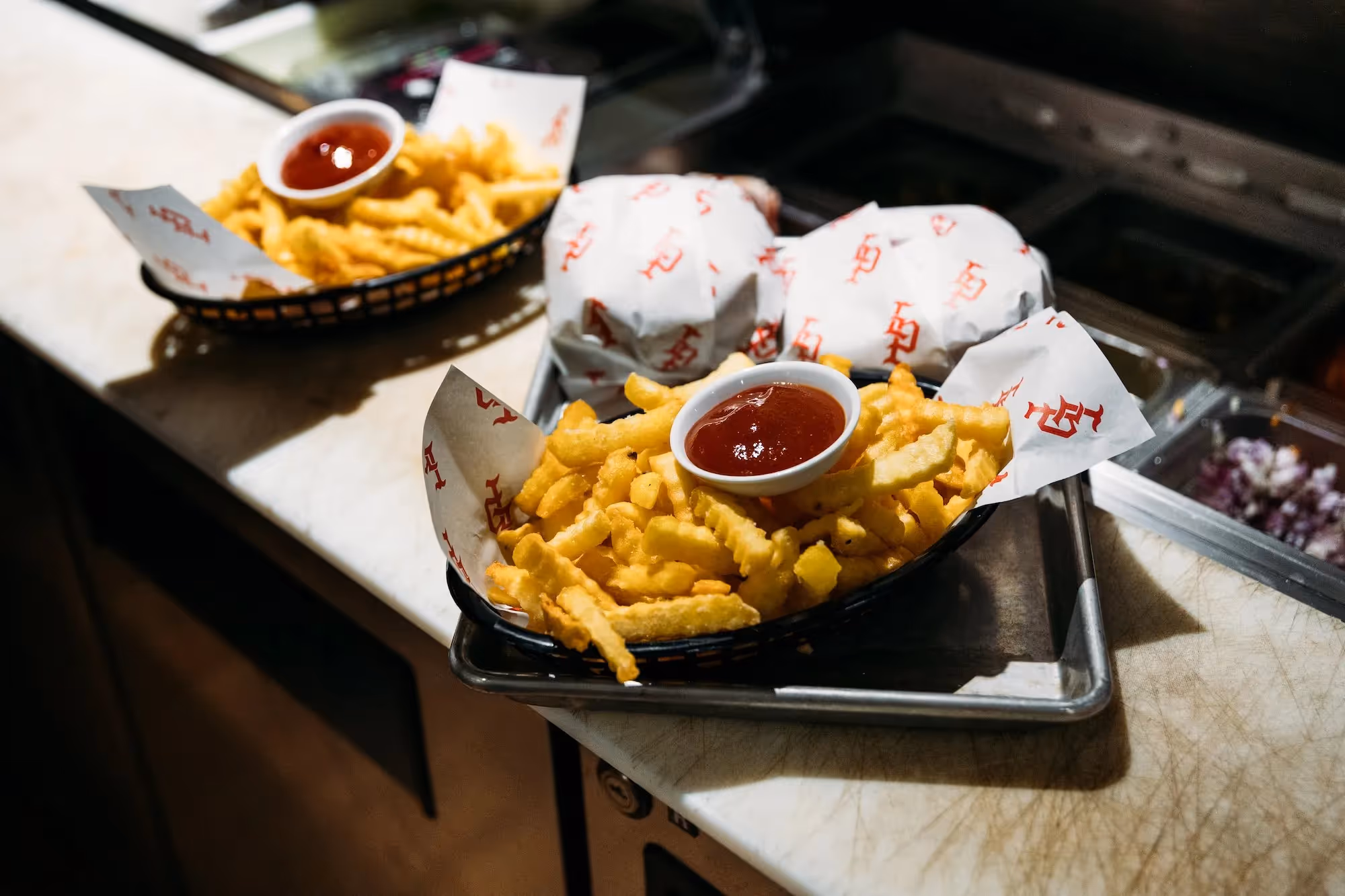 Delicious crinkle-cut fries served with ketchup, featured on a tray alongside wrapped burgers. Showcasing Hamilton's local dining scene, perfect for food lovers exploring the heart of the city. Support local eateries and enjoy community flavours.