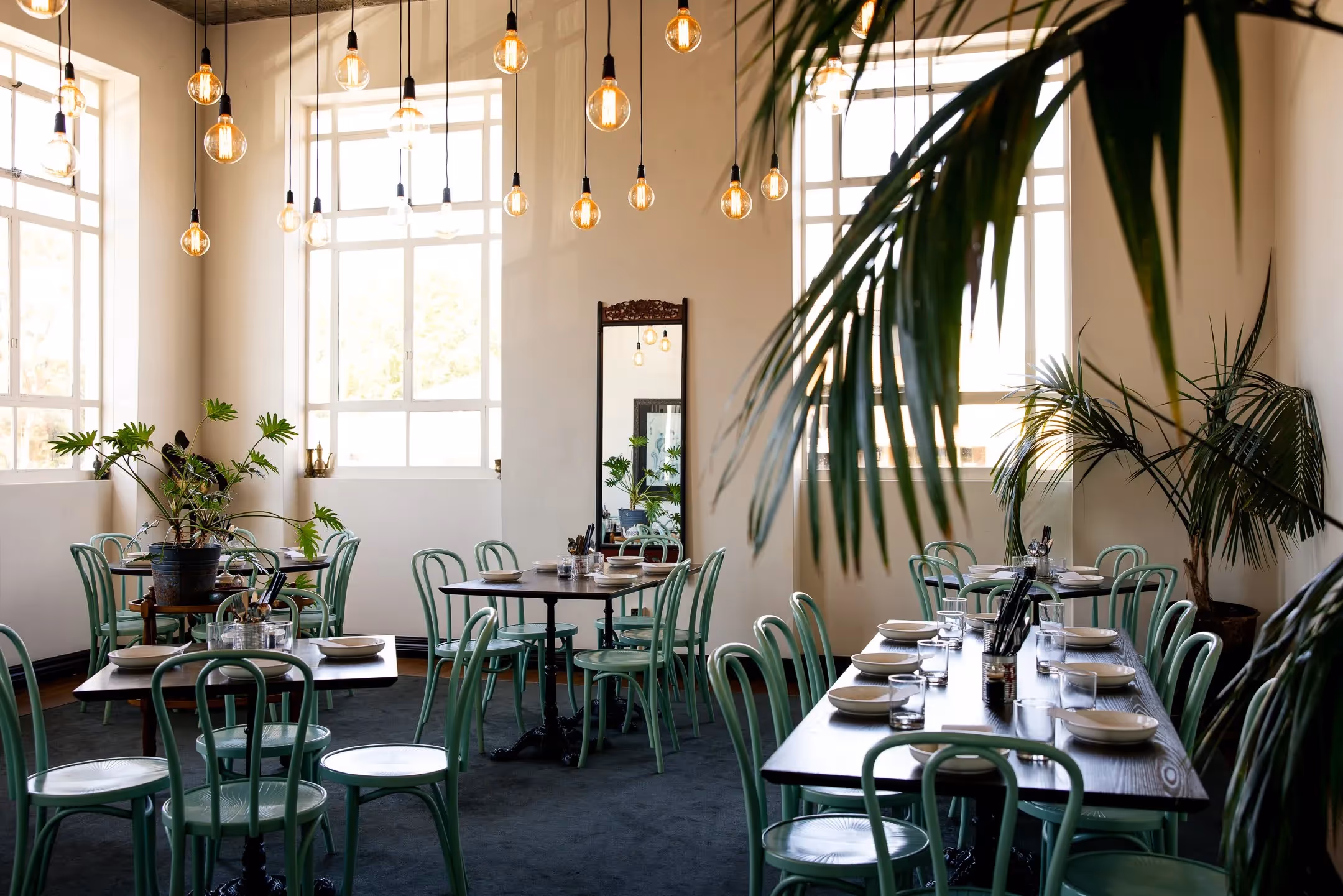 Alt text: A stylish dining area in Hamilton featuring green chairs and indoor plants, illuminated by pendant lights. This inviting space highlights local dining experiences, perfect for enjoying community gatherings and supporting local businesses.