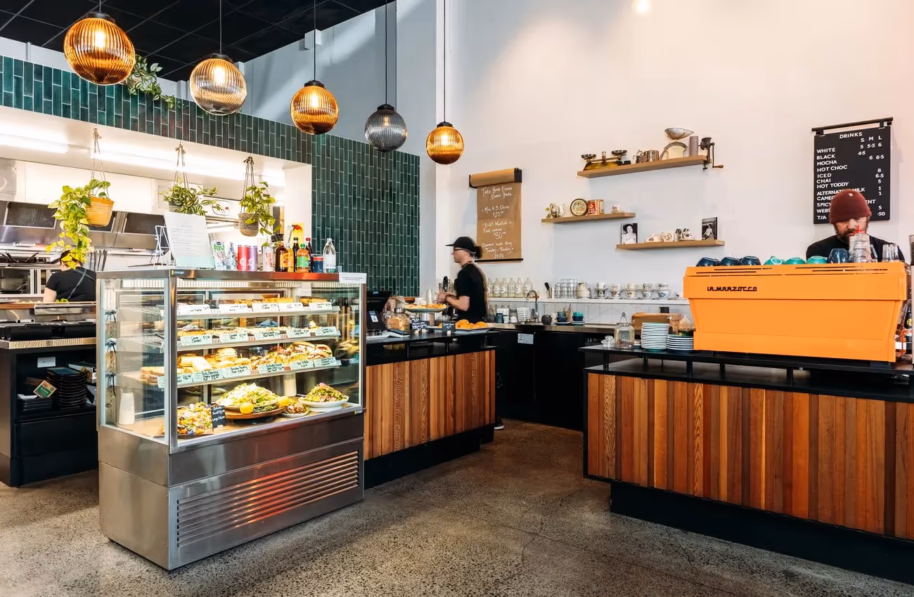 Alt text: A vibrant cafe in Hamilton showcasing local cuisine, featuring a glass display of fresh pastries and a stylish coffee machine. The welcoming atmosphere highlights support for local businesses and community experiences.