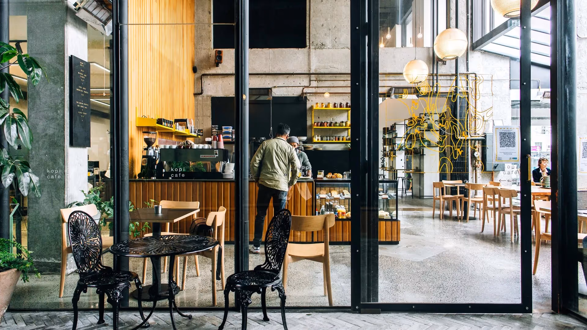 Alt text: "A modern café in Hamilton with a stylish interior featuring wooden finishes and large windows. Patrons enjoy a vibrant atmosphere while supporting local businesses at this community hotspot, perfect for coffee lovers."