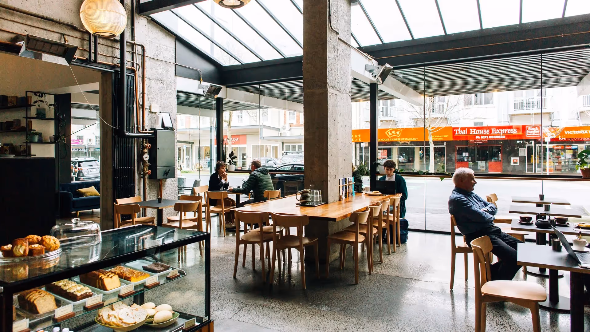 Alt text: Interior view of a modern café in Hamilton showcasing natural light, with patrons enjoying pastries and coffee. The café features sleek design elements and a view of local shops, highlighting the vibrant community spirit of Hamilton.