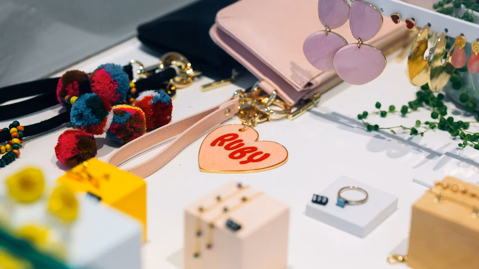 Alt text: A vibrant display of local jewellery and accessories in Hamilton, featuring colourful pom-pom keychains, pink earrings, and a personalised keyring. Emphasising unique, handmade products that showcase Hamilton's local artisans and businesses.
