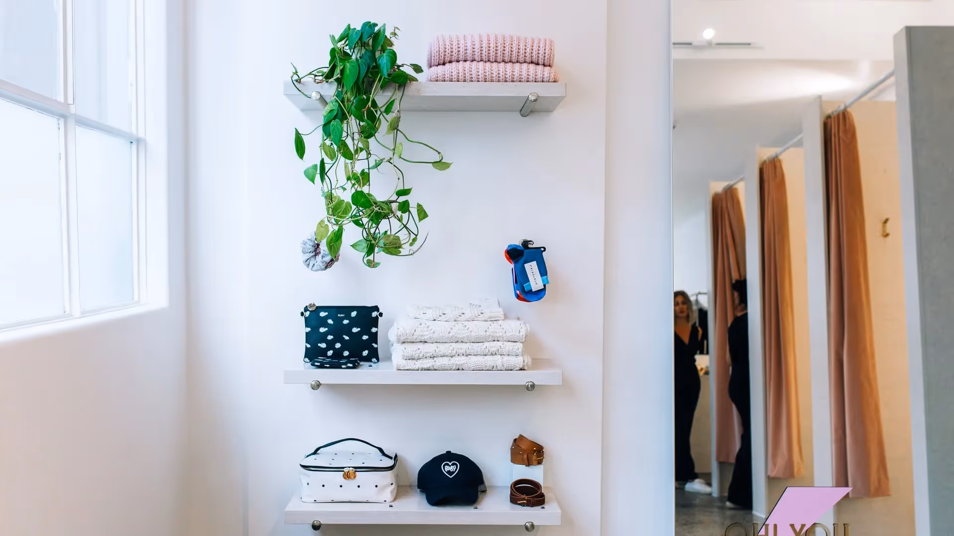 Alt text: "Stylish display of local products featuring folded textiles, accessories, and a potted plant. Showcasing Hamilton's best in a welcoming space, supporting local businesses and community experiences."