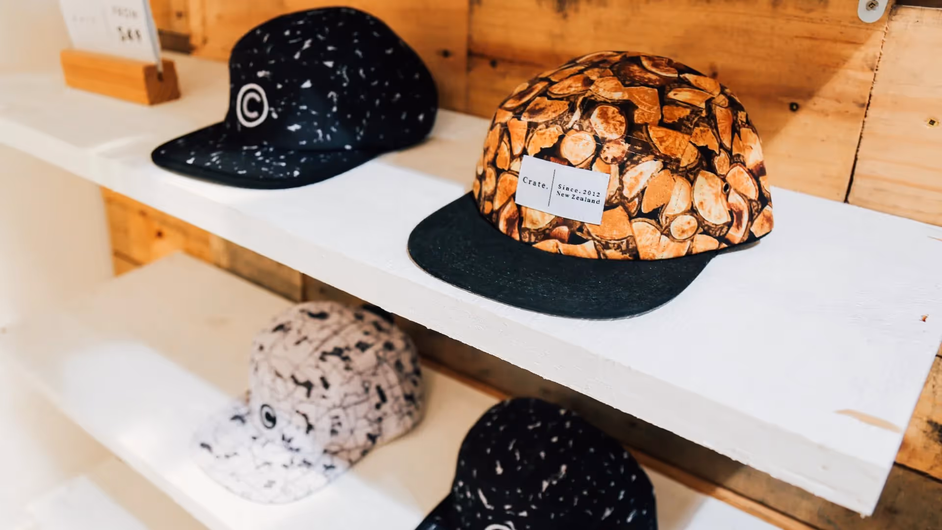 Alt text: A display of trendy caps featuring unique designs, including a wood-patterned cap and black speckled styles, showcased in a local Hamilton shop. Celebrate Hamilton's local businesses and fashion with these stylish accessories.