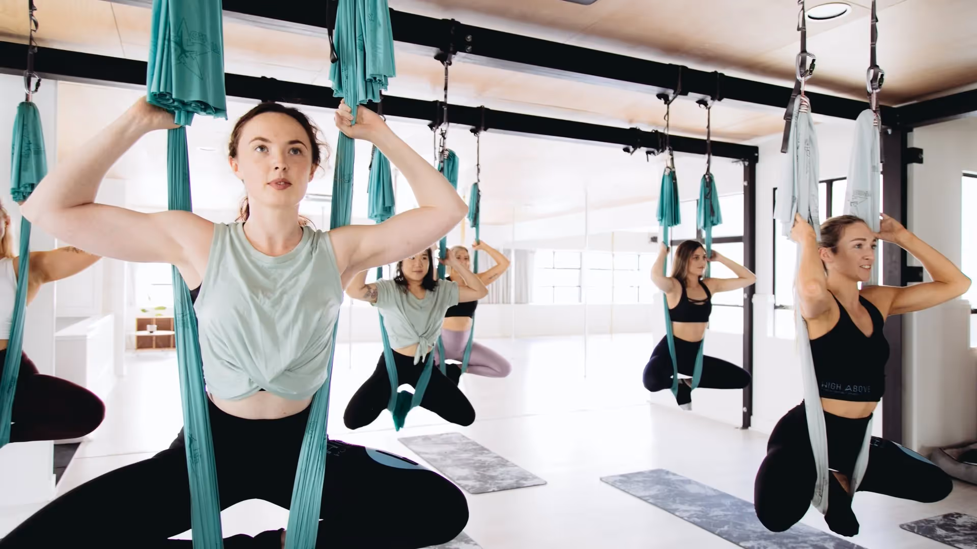 Alt text: Group of women participating in aerial yoga class at a modern studio in Hamilton. They use silk hammocks for support, showcasing wellness and fitness in the community. Love the Centre promotes local health and fitness experiences.