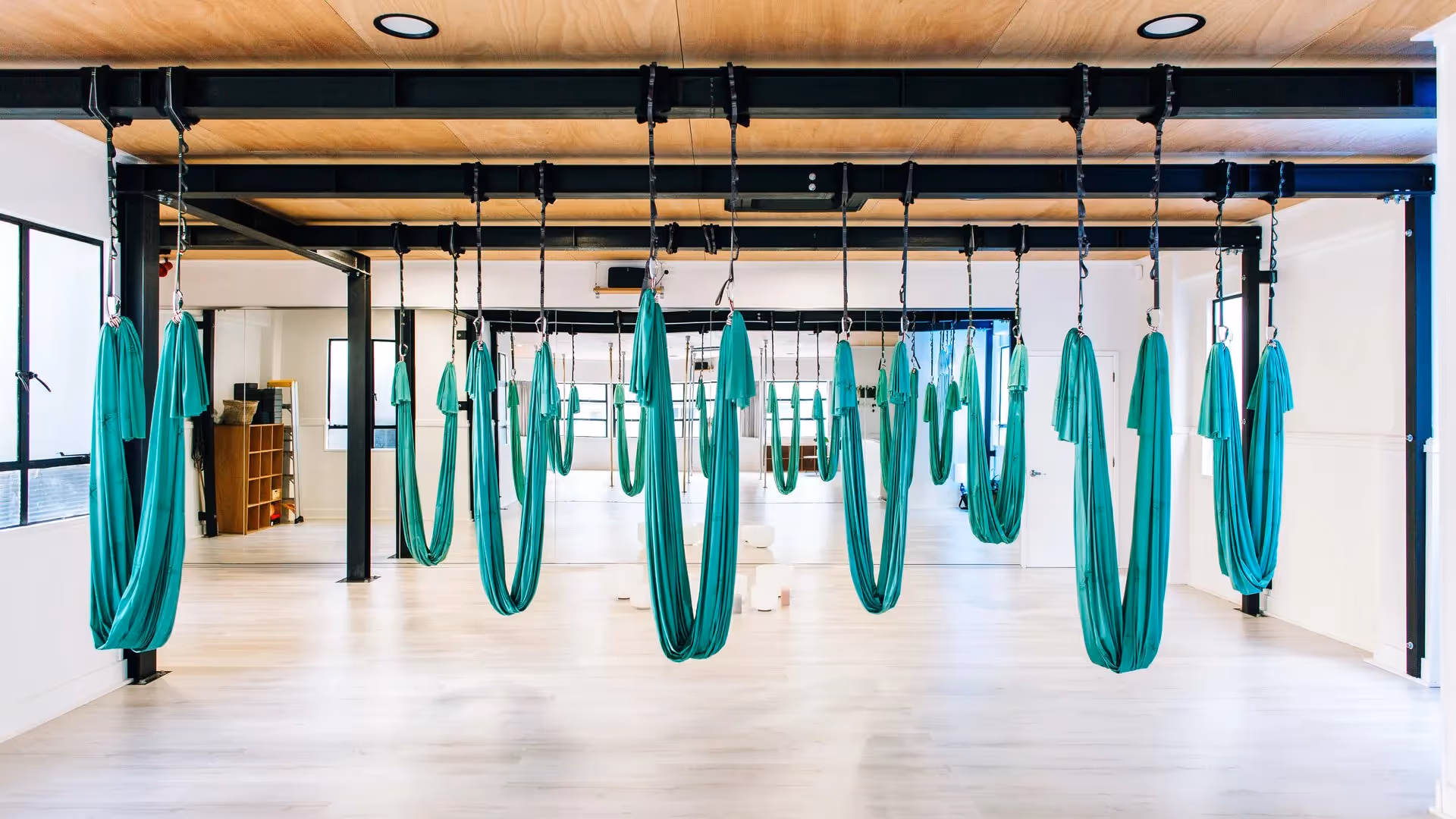 Alt text: A bright and airy aerial yoga studio in Hamilton featuring hanging green hammocks. The space promotes wellness and fitness, supporting local businesses by offering unique community experiences in the heart of the city.