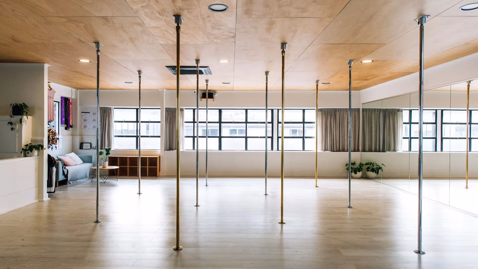 Alt text: "Spacious pole dancing studio in Hamilton with polished wooden floors and multiple vertical poles. Large windows allow natural light, creating an inviting atmosphere for fitness classes and community events. Perfect for local business promotion."