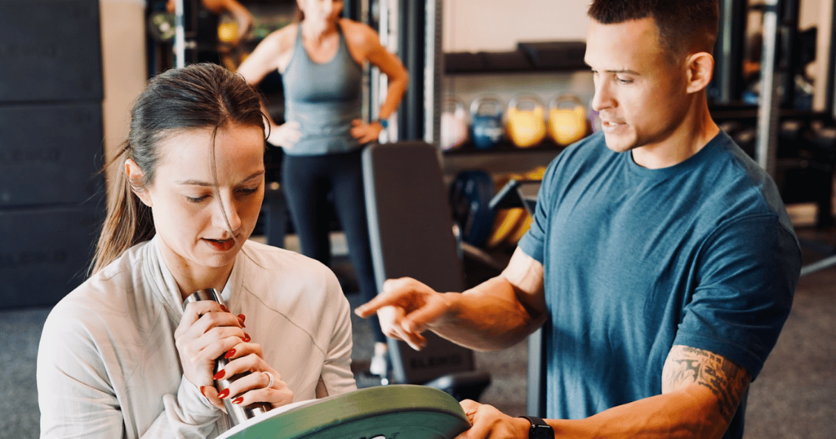 A coach guiding a member in her forties through a weighted plate hold