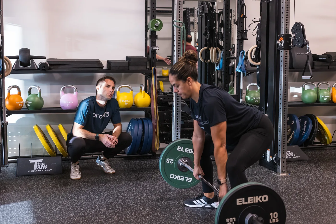 A proof3 coach watching a member deadlift, checking her setup before adding load