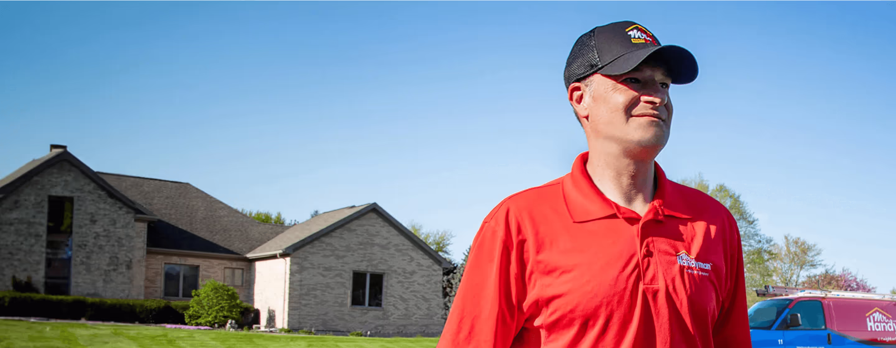 A man in a red shirt and hat standing in front of a house.