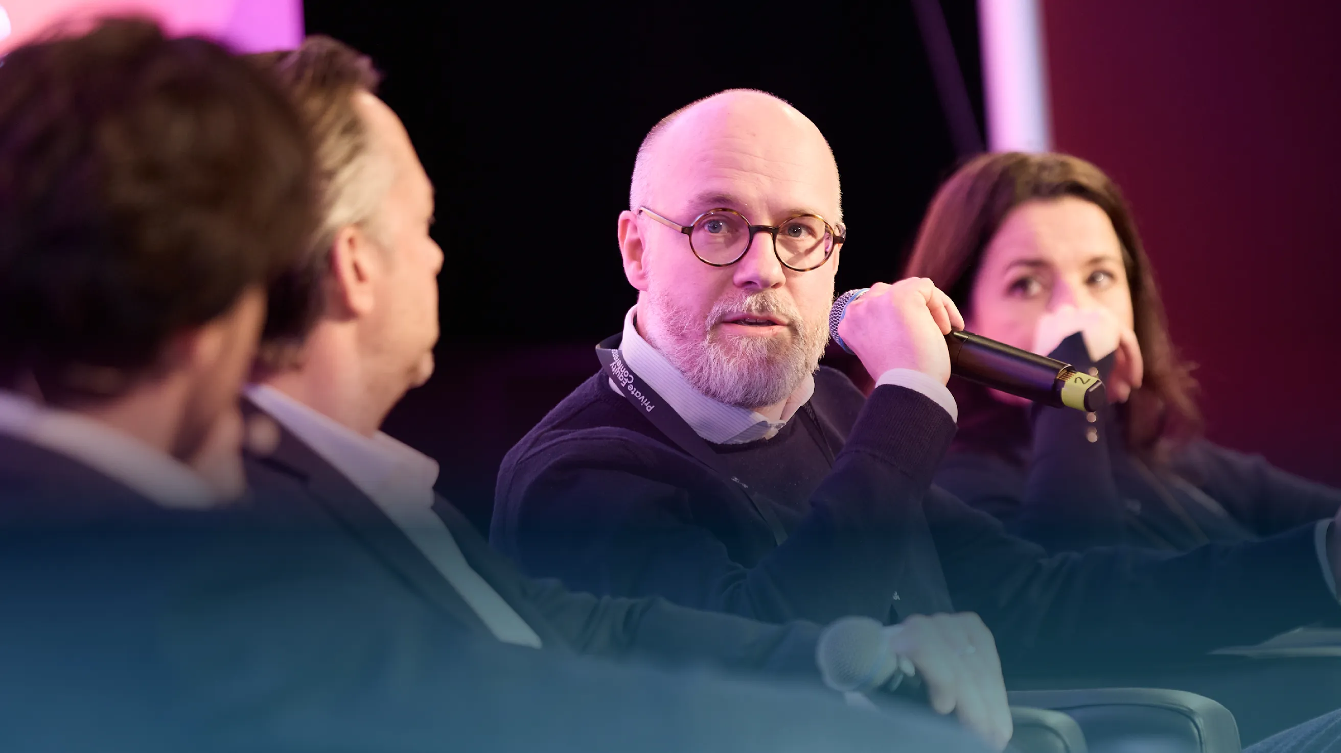 Panel discussion with a man holding a microphone speaking, accompanied by two other participants, one wearing a face mask.