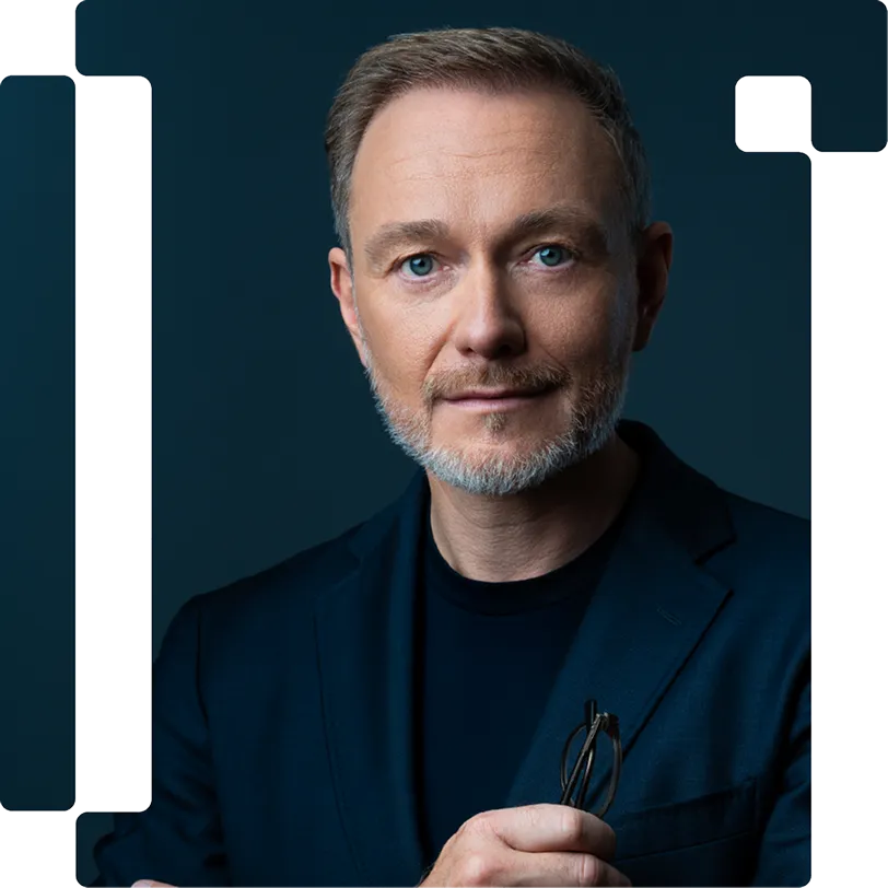 Portrait of Christian Lindner, wearing a dark blazer and holding glasses.