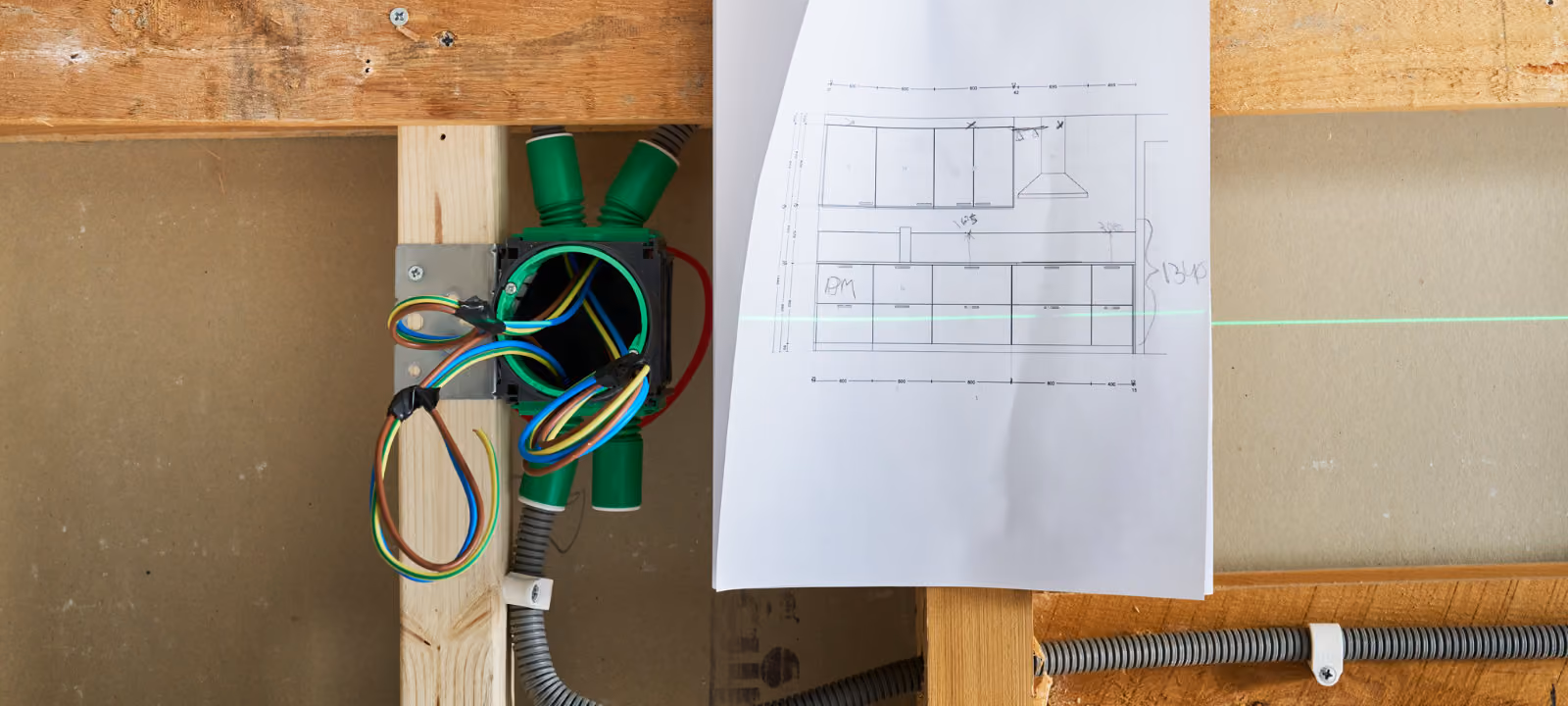 Elektriska ledningar och kabelrör monterade på trästomme med byggnadsritning och laserlinje.