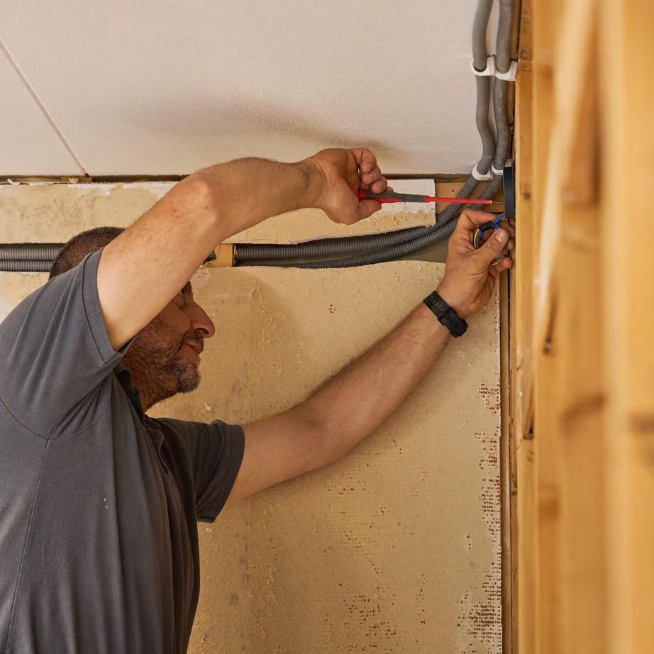 Man arbetar med elinstallationer inomhus med skruvmejsel och kablar.