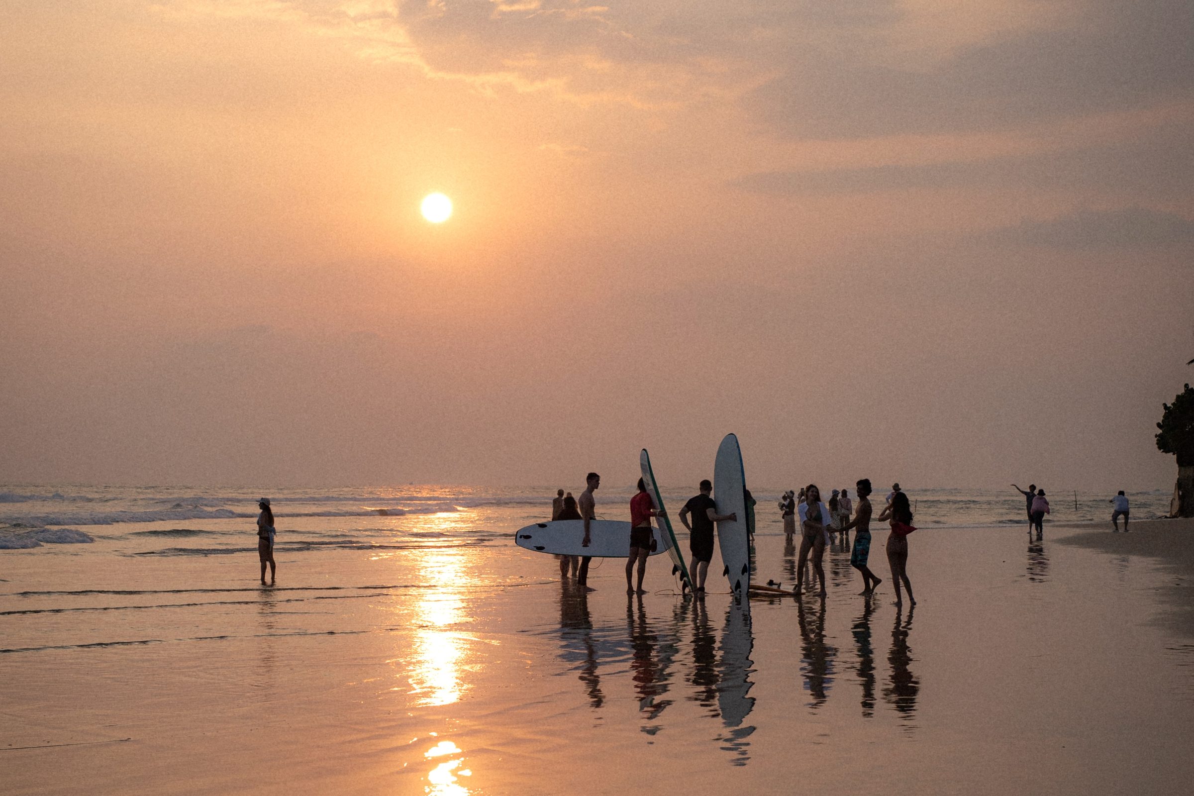 A group of surfers on the beach at sunset