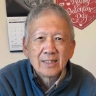An elderly Asian man wearing a blue shirt and smiling.