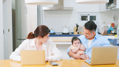 Eltern arbeiten an Laptops, während sie ihr Baby betreuen. Bild zur Darstellung der Vereinbarkeit von Familie und Beruf.