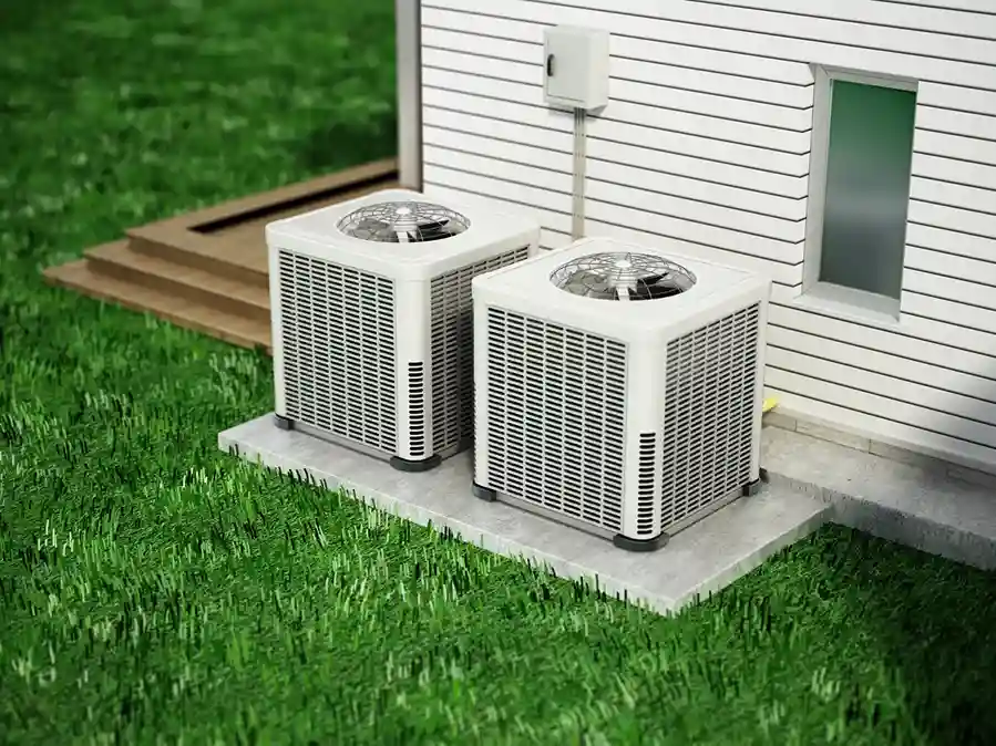 Two square outdoor heat pump units on concrete pads next to a house.