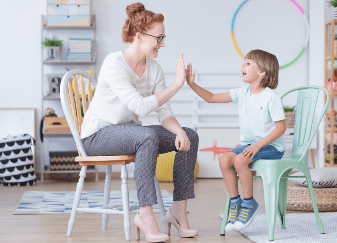 Speech, occupational therapy and psychotherapy Therapist and child sharing a high five during a therapy session