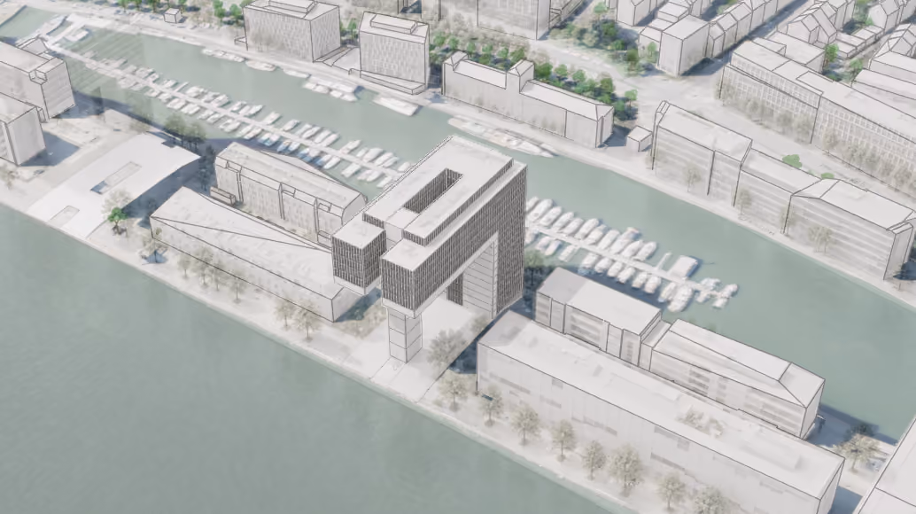 Aerial architectural rendering of a waterfront area featuring several modern buildings including a distinctive large building with a rectangular frame shape, surrounded by water and docks with boats. Trees line the waterfront promenade, and additional buildings appear across the street on the opposite side of the water channel.
