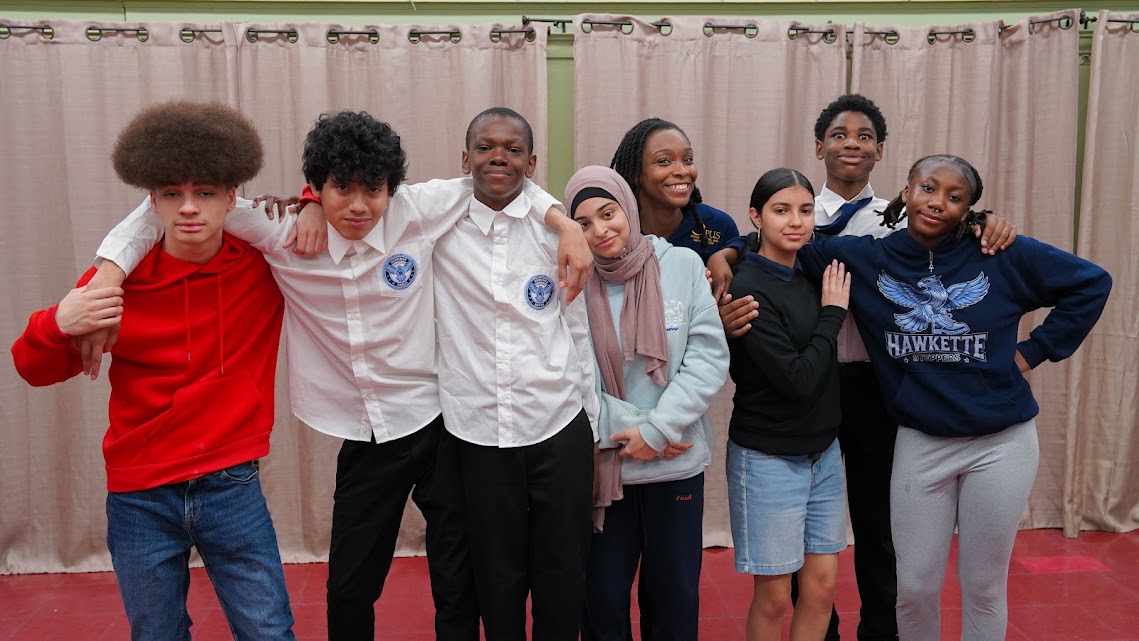 Group of eight diverse students posing together smiling at school