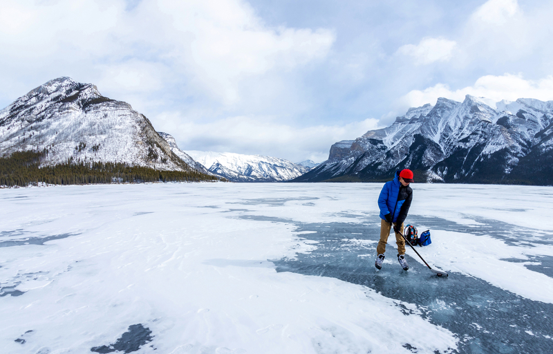 Boy enjoying ice hockey on frozen Lake Minnewanka in the beautiful winter at Banff National Park. Boy practicing ice hockey on frozen Lake Minnewanka in the Canadian Rockies of Banff National Park during the cold Winter.
