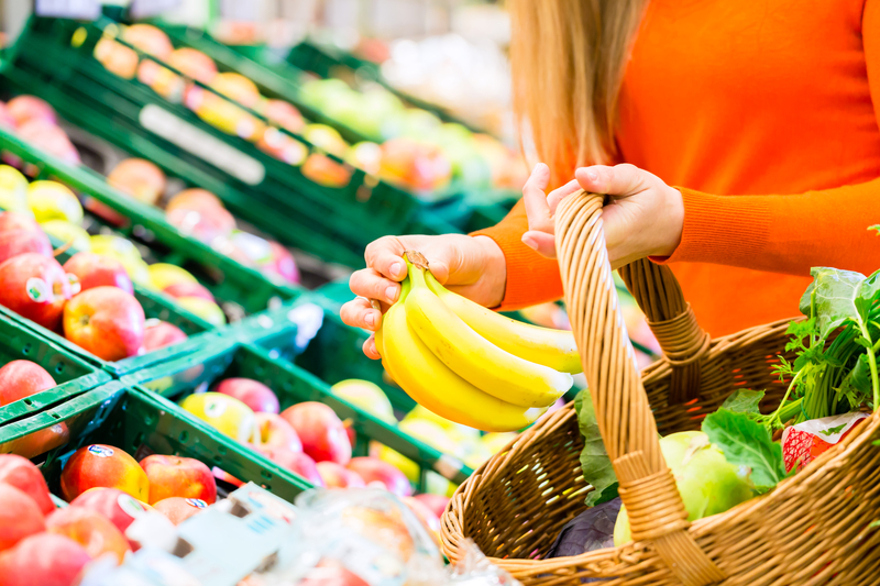 Woman in supermarket at the fruit shelf shopping for groceries, she is putting a banana in her basket. 