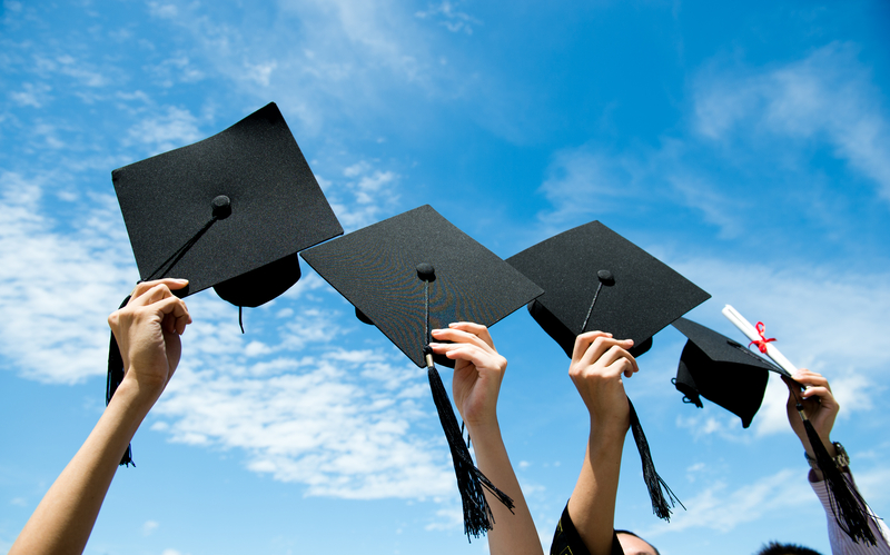Many hand holding graduation hats on background of blue sky.